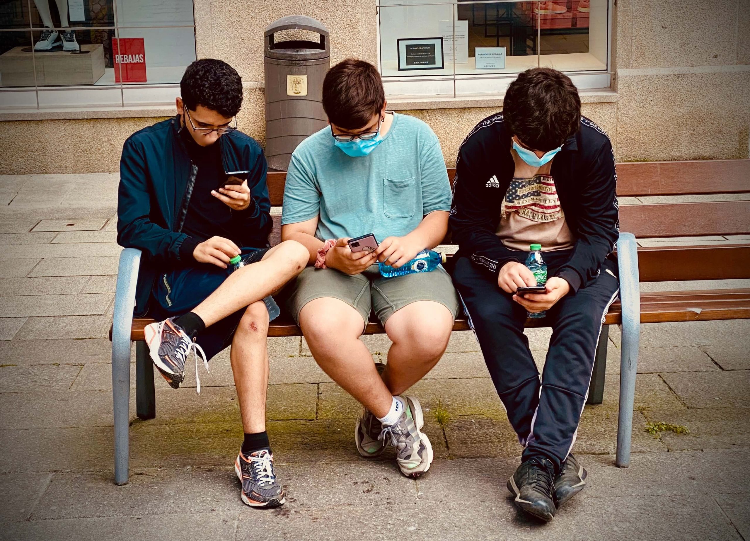 jóvenes sentados en banco con móviles