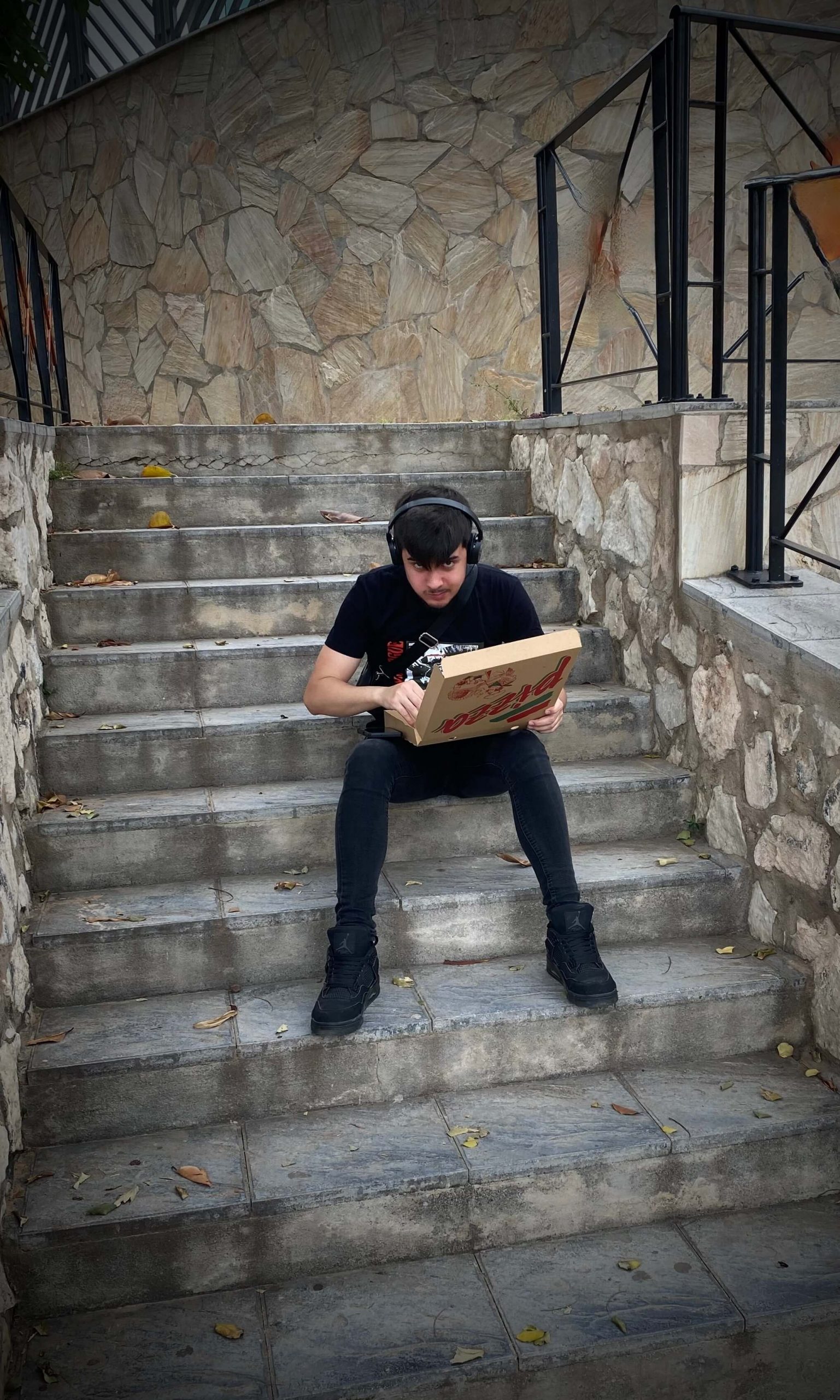 chico oyendo música con cascos y comiendo pizza en la calle